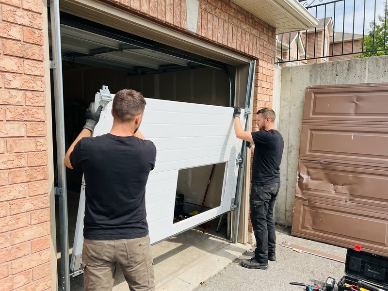 Two technicians fitting a replacement garage door panel