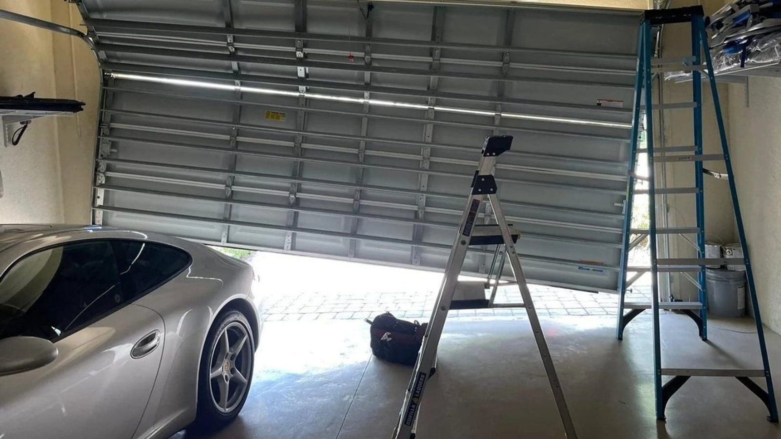 A ladder beside a raised sectional door and parked car